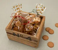 Trälåda med tre genomskinliga påsar fyllda med blandade kakor, knutna med rött och grönt snöre och dekorerade med guldfärgade hjärtan. Några runda kakor utanför lådan.