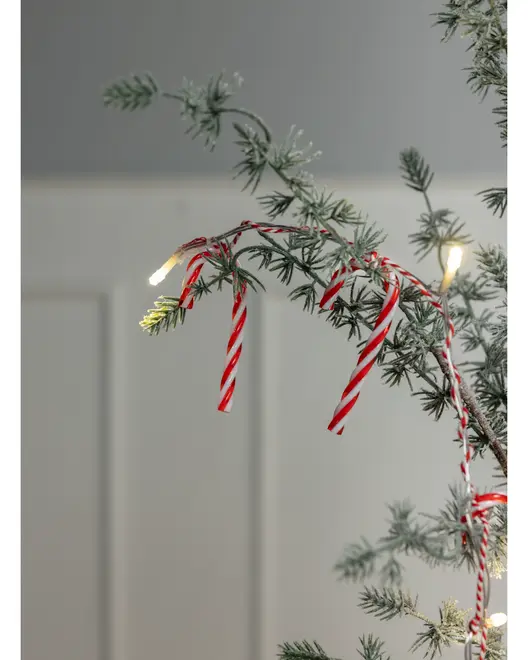 Kunstig juletræsgren med rød- og hvidstribede slikstokke og varme hvide LED-lyskæder. Grenene har et frostet, sneklædt udseende for en hyggelig julestemning.