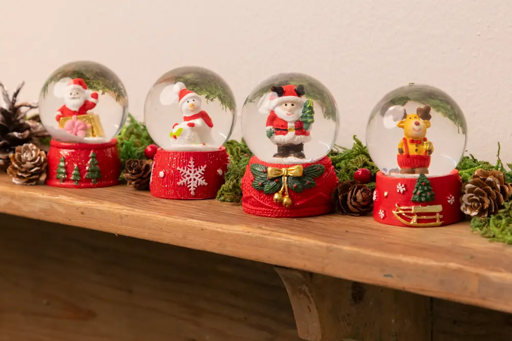 Fyra juliga snöglober med tomte, snögubbe, björn och ren i glaskupor, alla med röd bas dekorerad med julmotiv.