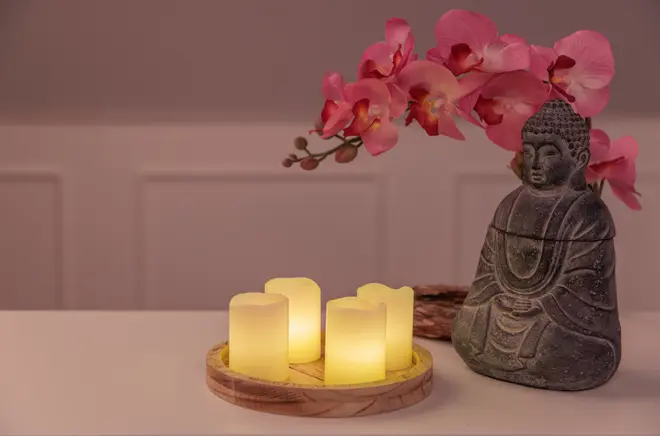 Set med fyra flamfria LED-ljus på träbricka, tillsammans med en Buddha-staty i sten och rosa konstgjorda orkidéblommor, perfekt för heminredning och lugn stämning.