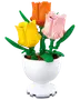 Tre LEGO-liknande tulpaner i gult, rosa och orange med gröna stjälkar och blad, arrangerade i en vit piedestalvas.