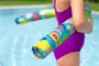 Farverig poolnudel med frugtmønstre, lavet af skum, let og fleksibel, ideel til svømning eller leg i vandet. Holdes af person i lilla badedragt ved pool.