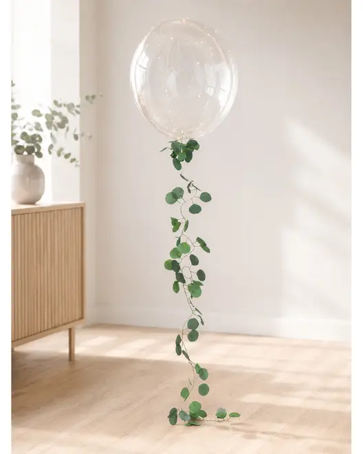 Genomskinlig ballong med lång hängande grön eukalyptusranka, som skapar en elegant minimalistisk fest- eller barnrumsdekoration. - Billedet er skabt med AI