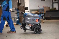 Bærbar generator med store hjul, solidt håndtag og flere strømudtag. Robust design til nem transport og udendørs brug, ideel til værktøj eller strøm under strømafbrydelser.