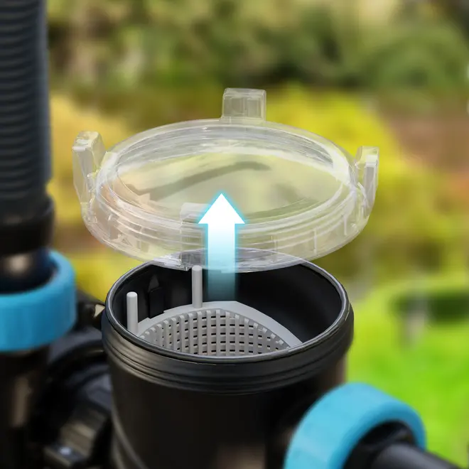 Nærbillede af gennemsigtigt plastfilterlåg, der løftes af sort cylindrisk filterhus med perforeret indvendig kurv. Bruges til vandfiltreringssystemer. Blå beslag ses på siderne.