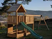 Udendørs legetårn i træ med overdækket platform, grøn rutsjebane, to gynger og sandkasse under. Egnet til børn, robust konstruktion, naturlig træfinish til haven.