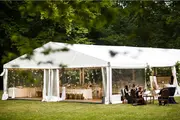 Stor hvid festtelt med gennemsigtige sider, opstillet udendørs på græs, dekorerede borde og stole indeni, ideel til bryllupper eller fester, omgivet af træer.