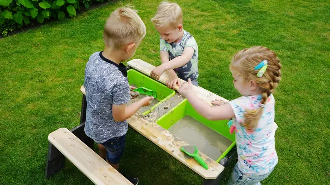 Udendørs mudderkøkken til børn med to grønne plastbaljer, træbænke og legetøjsredskaber. Perfekt til sanseleg i haven, stimulerer fantasi og kreativitet.