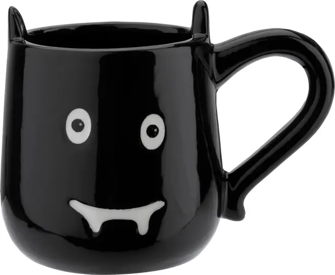 Svart keramikmugg med vampyransikte, vita ögon, huggtänder och två spetsiga öron på kanten. Rolig, unik mugg perfekt för Halloween eller temadrycker.