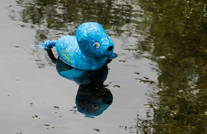 Blå plastikand formet som et badelegetøj med marmoreret finish, flydende på vand. Har tegneserieøjne, flad næb og hale, velegnet til udendørs leg i vand.