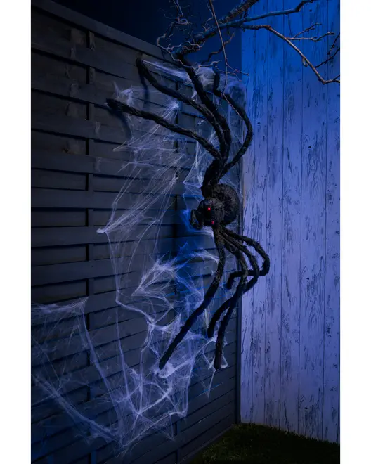 Stor svart Halloween-spindel med röda ögon, långa böjbara ben och vitt spindelnät, perfekt för utomhusdekoration på vägg eller staket. Skapar en skrämmande effekt.