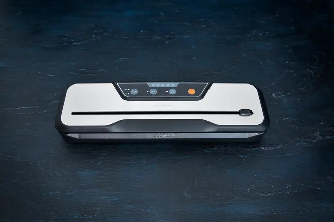 Elegant vakuumforsegler med hvid top, sorte kanter og kontrolpanel med knapper og indikatorlys. Bruges til at forsegle madposer og bevare friskhed.