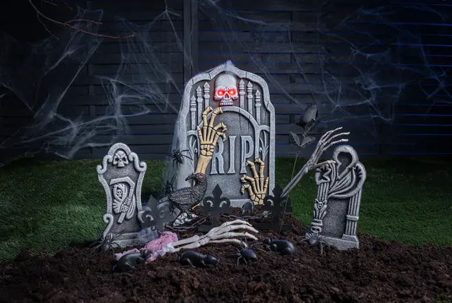 Halloween gravplatsdekoration med tre gravstenar, skelett-händer, dödskalle, råttor, spindlar och spindelväv. Mittenstenen har "RIP" och lysande röda ögon.