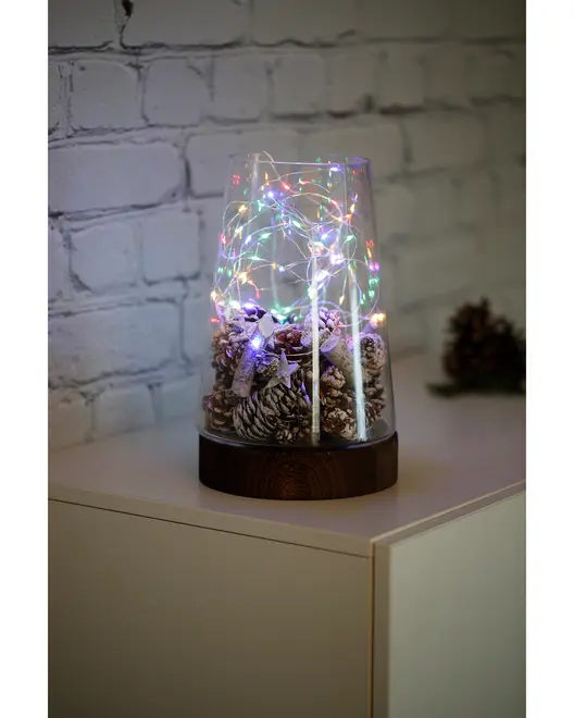 Glaskuppel med frostede kogler og flerfarvede LED-lyskæder på mørk træbase, ideel som dekorativt midtpunkt til hjemmet eller juleudsmykning.