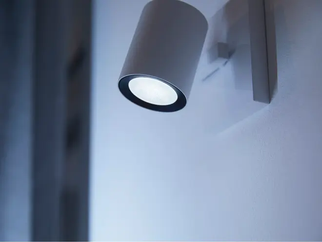 Moderne vægmonteret spotlampe med cylindrisk hvidt metalhus, udsender klart hvidt lys. Har en firkantet base til sikker montering, velegnet til accent- eller læsebelysning.