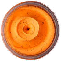 Slät, orangefärgad röra eller dipp i glasburk, med synliga örter och kryddor, krämig konsistens, troligen smaksatt hummus eller grönsaksbaserad röra.