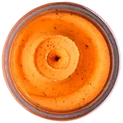 Cremet, orangefarvet dip eller smørepålæg i glas, med synlige krydderurter og krydderier, jævn konsistens, sandsynligvis smagstilsat hummus eller grøntsagsbaseret smørepålæg.