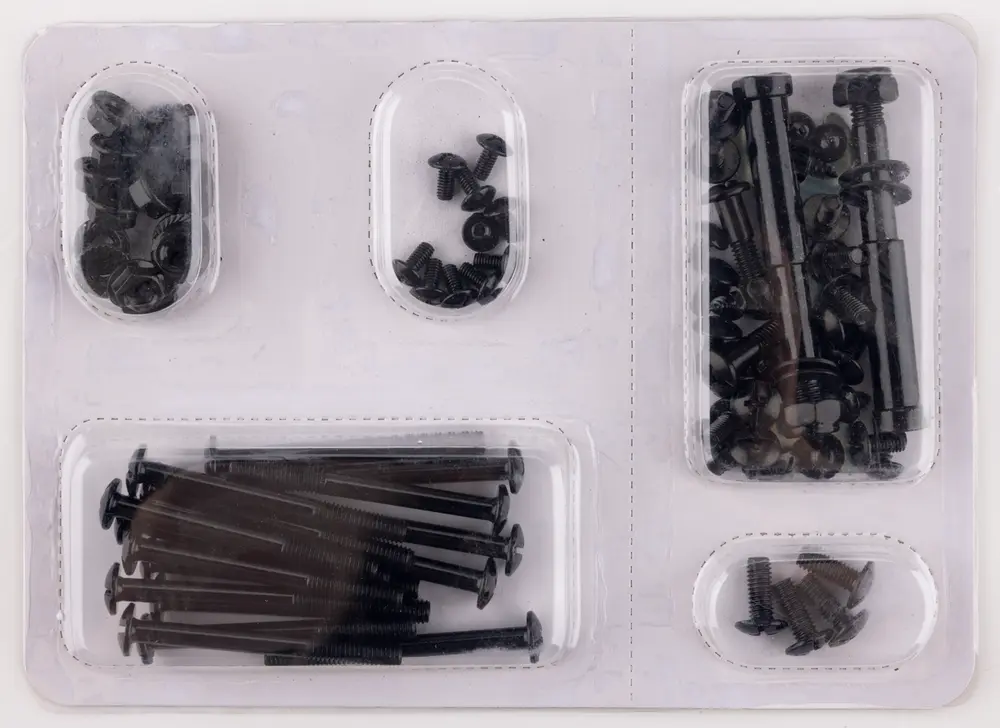 En gennemsigtig plastpakke med et udvalg af sorte metalbeslag, herunder bolte, møtrikker og skiver i forskellige størrelser. Beslagene er organiseret i separate rum, hvor hvert rum indeholder en bestemt type eller størrelse. Boltene har enten runde eller sekskantede hoveder, og møtrikker og skiver passer til boltene. Præsentationen er overskuelig og gør det nemt at identificere de enkelte dele.