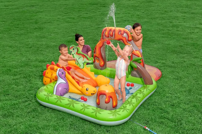 Oppustelig børnepool med dinosaurtema, rutsjebane, vandsprøjte og farverige bolde. Har palmetræer og vulkanmotiver, ideel til udendørs vandleg for små børn.