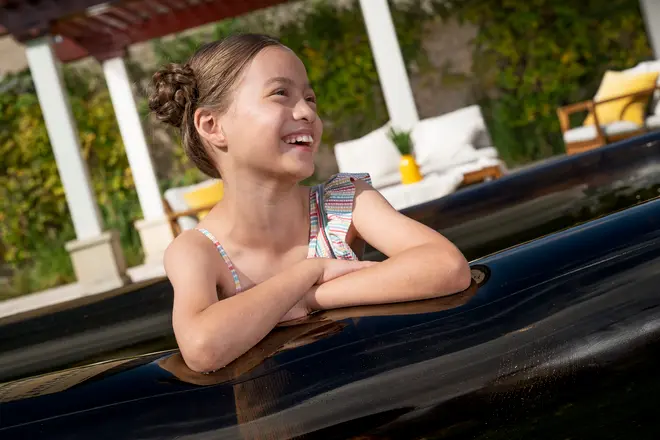 Barn i stribet badedragt sidder i et sort spabad udendørs. Spabadet har blank overflade, og baggrunden viser havemøbler og grøn beplantning.
