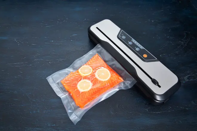 Vakuumpakker med kontrolpanel, forsegler en pose med frisk laksefilet og citronskiver. Kompakt, rektangulært design, ideel til madopbevaring og sous vide-tilberedning.