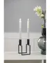 Modern svart metall-ljusstake med geometrisk fyrkantig bas, rymmer två höga vita kronljus. Minimalistisk design, ljusen är tända på bilden.