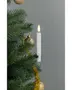 Batteridrevet LED-lys med hvidt stearinlys og varm gul flamme, fastgjort på en juletræsgren. Omgivet af grønne nåle, guldkugler og guldtinsel.