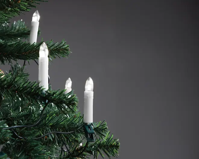 Sæt elektriske lys med hvide baser, fastgjort på kunstige grønne grene af juletræ, udsender varmt hvidt lys, ideel til indendørs juledekoration.