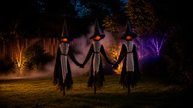 Tre uhyggelige Halloween-heksedekorationer med lysende græskarhoveder, sorte spidse hatte, flossede sorte dragter og hvide slør, holdt i hånden.