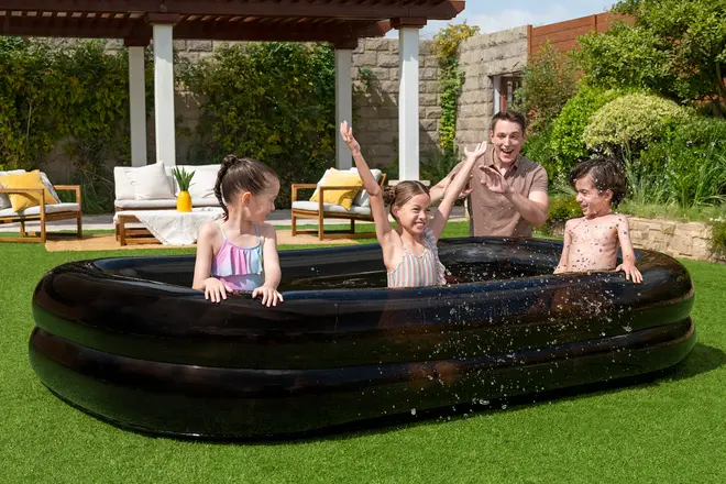 Stor sort oppustelig rektangulær pool til børn, placeret udendørs på græs. Har tre luftkamre for stabilitet og holdbarhed. Perfekt til leg i haven om sommeren.