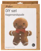 DIY-set för att göra en pepparkaksgubbe-kudde. Brun plysch, röd fluga, vita knappar, leende ansikte. Färdig storlek: 29 x 36 cm. Från 6 år.