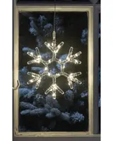 A decorative snowflake-shaped light made from clear plastic tubing with integrated warm white LED bulbs. The snowflake has six symmetrical branches and is suspended by a transparent cord, designed for hanging in a window. The lights emit a soft, festive glow, ideal for holiday or winter-themed decor.