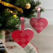 Rødt og hvidt flettet julehjerte af papir med prikker og striber, hænger på juletræet med en papirhank. Traditionel dansk julepynt.