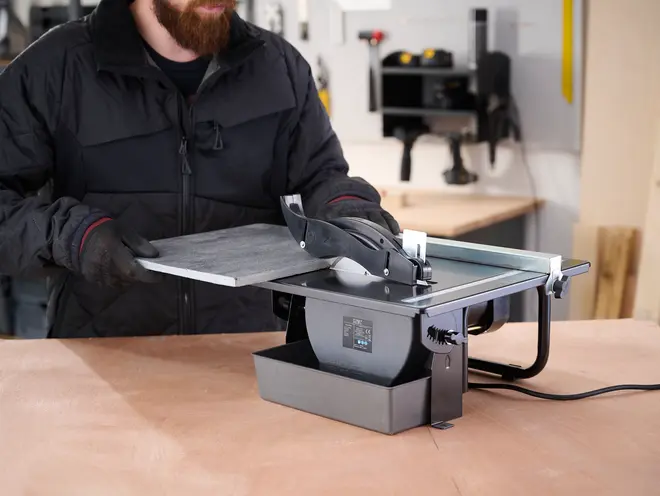 Elektrisk fliseskærer med vandbakke, rund diamantklinge, justerbar skæreguide og robust metalramme. Perfekt til præcis skæring af keramiske eller stenfliser på værkstedet.