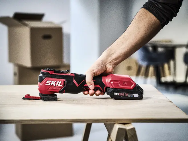 Rød og sort SKIL trådløs oscillerende multiværktøj med 20V PWRCORE batteri, ergonomisk greb og tilbehørsmontering, velegnet til skæring, slibning og skrabning af forskellige materialer.