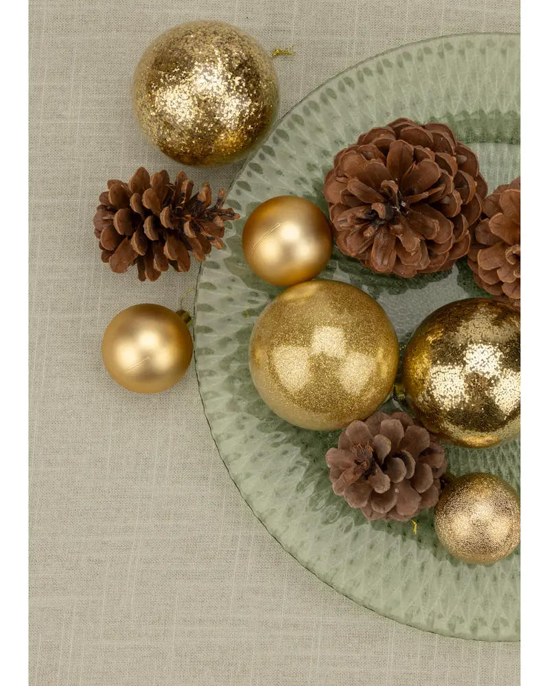 Set med gyllene julgranskulor i matt och glitter, tillsammans med naturliga bruna kottar på en texturerad glasplatta. Perfekt för festlig dekoration.