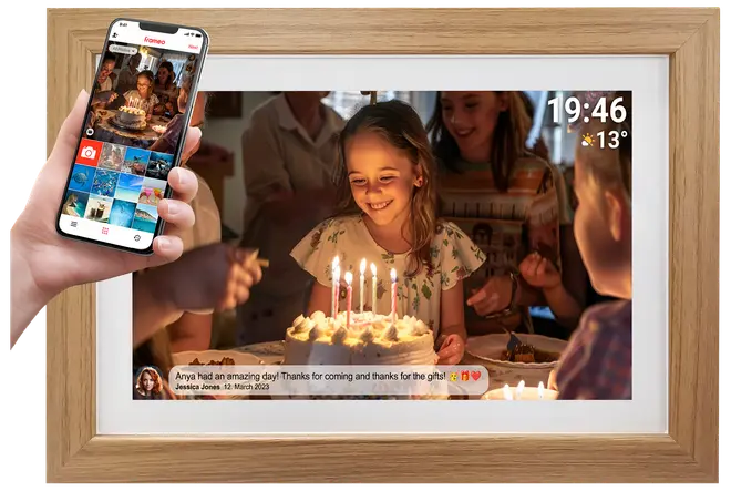 Digital fotoram med ljus träram, visar en födelsedagsscen. Visar tid, väder och meddelande. En hand håller en smartphone för fotodelning.