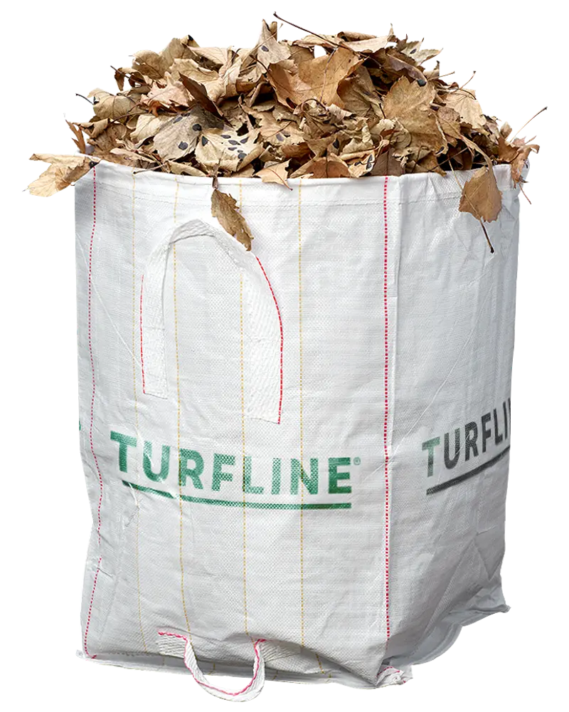 Stor hvid vævet polypropylen havesæk med håndtag, mærket 'TURFLINE', fyldt med tørre brune blade. Velegnet til haveaffald, blade eller græsafklip.