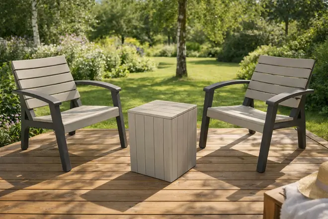 Utomhusmöbelset med två grå ribbade karmstolar och ett matchande fyrkantigt sidobord, tillverkade av väderbeständigt material, placerade på ett trädäck i trädgårdsmiljö.