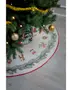 Rund julgransmatta med broderade grankvistar och festliga motiv, röd kant, placerad under granen med presenter. Krämfärgad bakgrund, dekorativ design för skydd av granens bas.