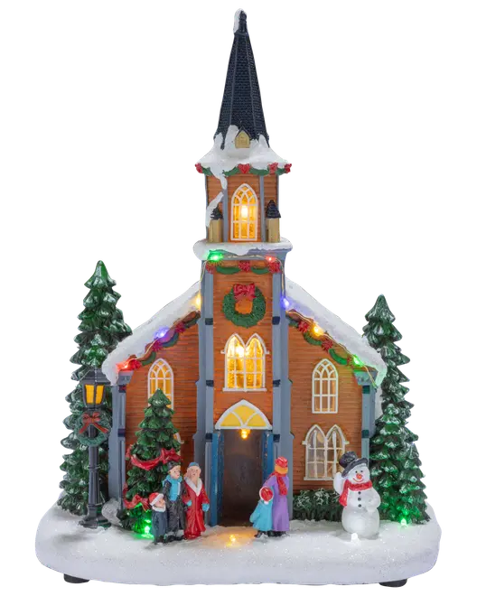 Oplyst julekirke med sneklædt spir, lys i vinduerne, grantræer, figurer, snemandsdekoration og farverige festlige lyskæder.