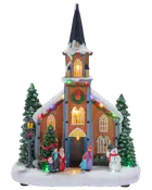 Oplyst julekirke med sneklædt spir, lys i vinduerne, grantræer, figurer, snemandsdekoration og farverige festlige lyskæder.