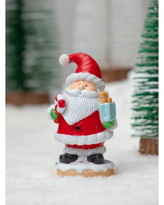 Festlig tomtefigur med röd dräkt, vitt skägg och luva, håller ett blått paket och polkagris, står på snöliknande bas. Perfekt som juldekoration.
