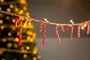 Rød- og hvidstribede sukkerstokke hænger fra en snor med små lys, sløret juletræ og gyldne lys i baggrunden, ideel til juledekoration.