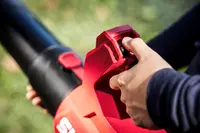 Röd och svart handhållen lövblås med ergonomiskt grepp och boost-knapp. Användarens hand trycker på kontrollen för extra kraft och luftflöde utomhus.