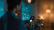 Person holder en smartphone med smart home-termostatstyring i et hyggeligt, blødt oplyst rum om natten.