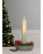 Högt vitt adventsljus med siffror, placerat i dekorativ skål med mossa, kottar och röda dekorationer. Fjärrkontroll ingår. Julgran i bakgrunden.