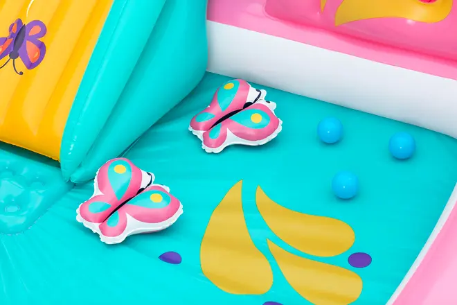 Oppustelig børnepool med farverige sommerfugle- og blomsterdesign, to sommerfugleformede legetøj og tre blå plastikkugler på turkis og gul bund.