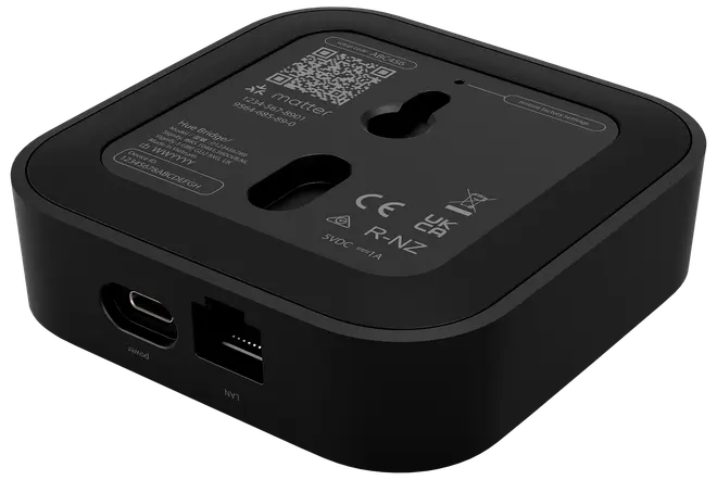 Sort smart home-hub med USB-C og Ethernet-porte, vægmonteringshuller og produktinformation på bagsiden. Kompakt, firkantet design til netværksforbindelse og integration af smarte enheder.