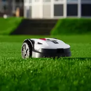 Hvid og sort robotplæneklipper med store baghjul, stående på en grøn græsplæne.